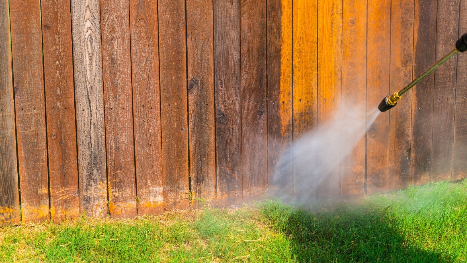 Power-washing a weathered wood fence to prep it before staining